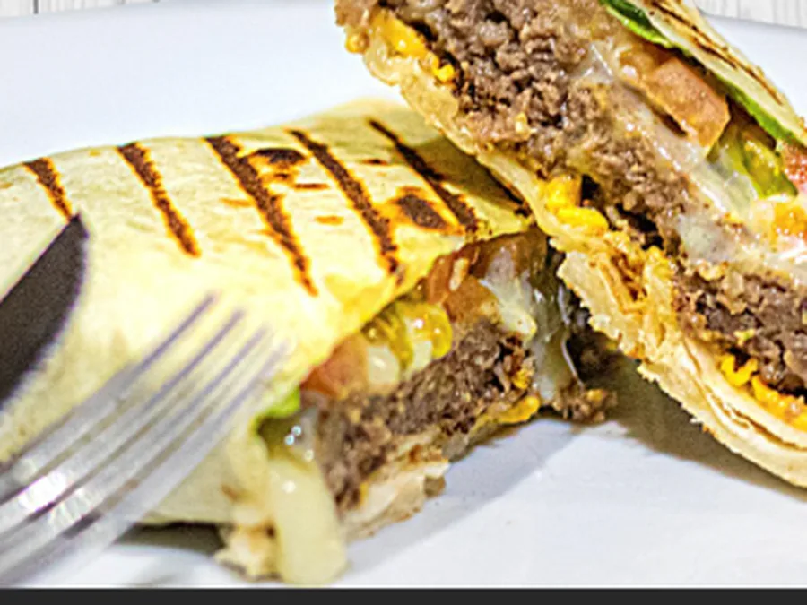 Hamburguesa árabe a la parrilla en tortilla de trigo, cortada por la mitad mostrando el relleno de carne y queso