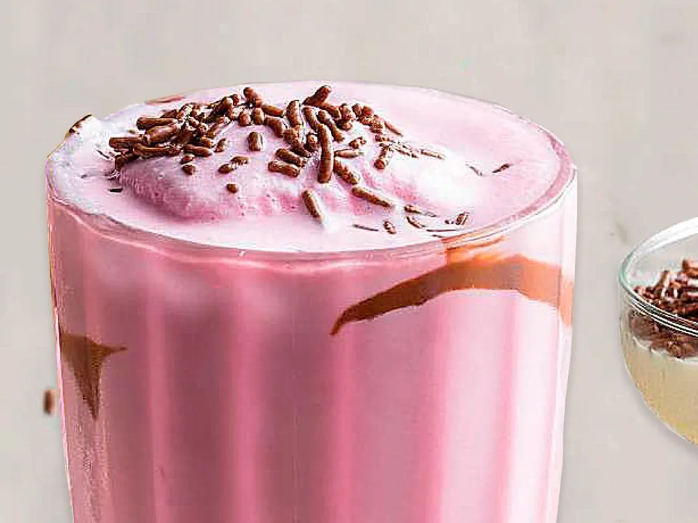 Malteada de fresa coronada con crema y chispas de chocolate en vaso de vidrio